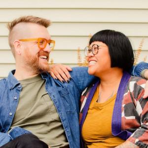 Two seated people smiling at each other with an arm around each other.