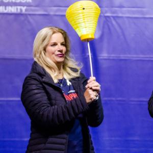 Rachel Howard holding a gold lantern. A person at a podium with a microphone beside her.