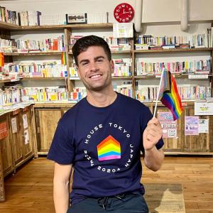 Javier Raya with a small pride flag in a room full of books.