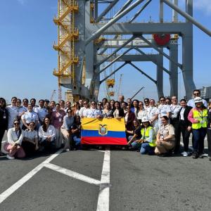 A large group of women and men stand together at a port terminal holding the Ecuadorian flag during a gender equity event with Red MAMLa.