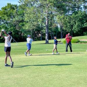 Black students practice their golf swings on a rolling green field