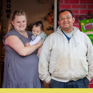 A smiling couple on their porch holding a baby