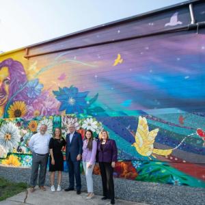 Group of people stood in front of a brick wall which has art on 