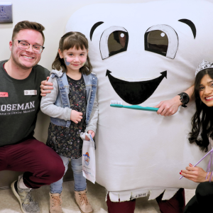 Two adults and a child next to a tooth mascot