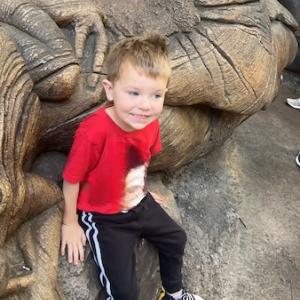 Rowan, smiling and seated on a wooden sculpture.