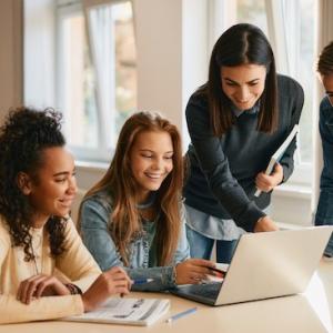 Teacher working with a group of four students who are seated behind a laptop.