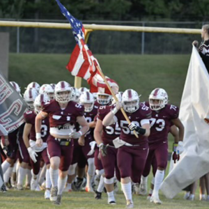 A football team running onto a field, one carrying an american flag.