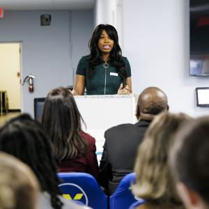 Photo: SCO client, Chrissa B. speaking at the podium and sharing from her journey, “I want my son to grow as much as I am.”
