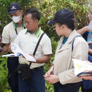 A group of six people outside looking at bird guide books. One carries a camera.