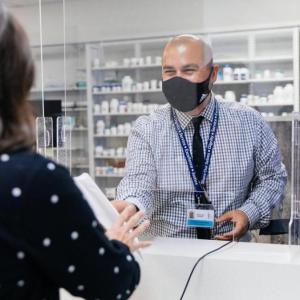 A pharmacy health worker hands a prescription to a patient.