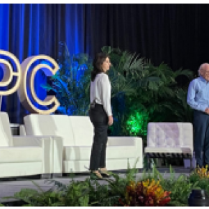 Two people on stage, couches and SPC behind them.