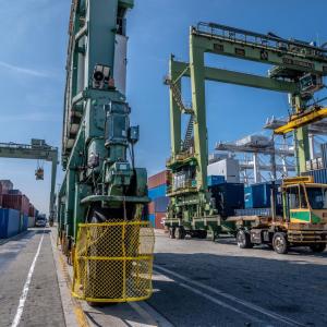 Crane truck moving along stacks of shipping containers.