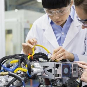 two people wearing lab coats and safety glasses working on a piece of equipment