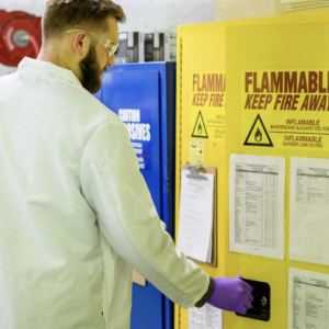 A person opening a yellow locker that has a fire hazard sign on the front of the door 
