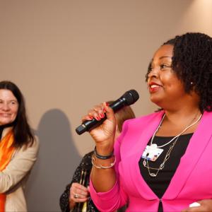 Salah Goss with a microphone, others to her side clapping and smiling.