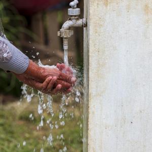 Hands being washed under outdoor faucet