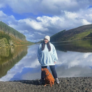 Sarah shown with her dog in front of a mountain lake.