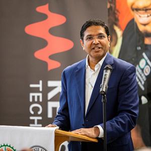 Satish Dhanasekaran standing at a podium with a microphone.