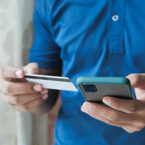 A person holding a credit card in one hand and using a cell phone with the other.