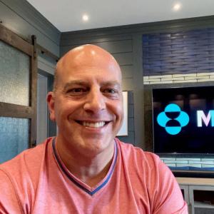 scott wright with a screen behind him playing the Merck logo in LGBTQ+ colors