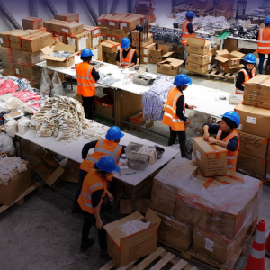 Women wearing safety helmets and high-visibility vests sort and pack materials inside a warehouse at ZEDE Posorja in Ecuador.