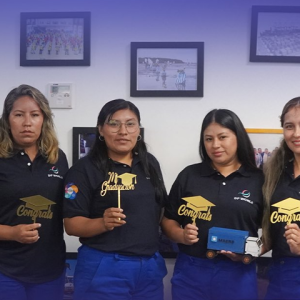 Five women wearing DP World uniforms hold graduation-themed signs during a recognition event for the Operadoras del Futuro program.