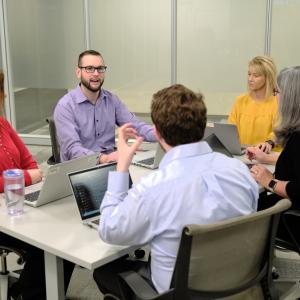 Richard McMichael, in a light purple shirt, at a conference table talking to coworkers