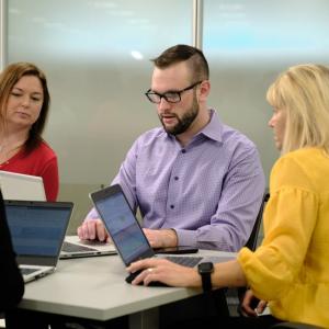 Richard McMichael works on his laptop while two coworkers look on