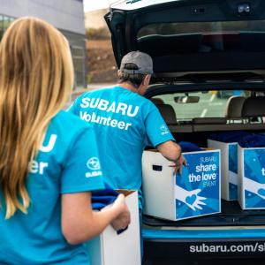 two Subaru volunteers loading donation boxes into the boot of a car