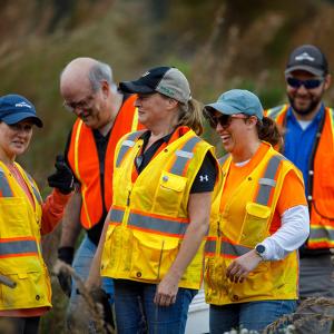 5 people laughing. They are outside, wearing high-vis vests and work wear.