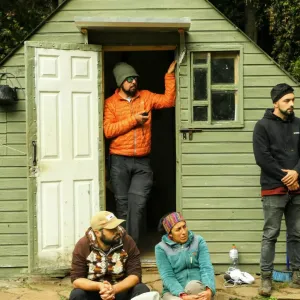 A green shed with a person stood in the doorway and another to the right, with two people sat on the floor