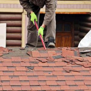 A person taking shingles off of a roof