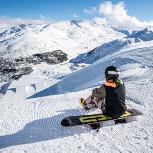 A person sat on a ski board at the top of a snowy mountain