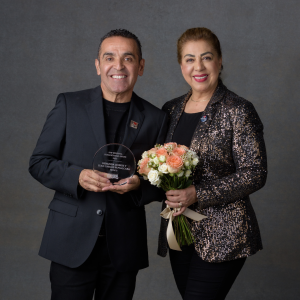 Two people stood next to each other smiling, one person holding an award and the other holding flowers