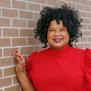 Stacey Bledsoe in a red shirt leaning against a brick wall.
