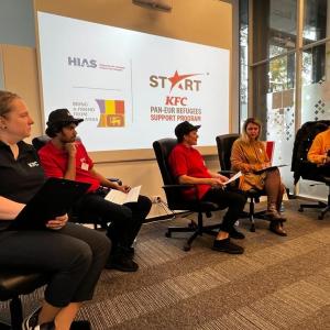 People seated in a room, some in KFC uniforms. "Start KFC" projected on a screen behind them. 