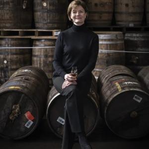 Stephanie MacLeod seated on a barrel, many barrels behind her.