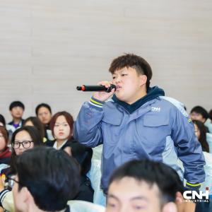 Person stood up in a crowd of people, talking into a microphone 