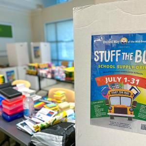A sign for "Stuff the Bus" next to a table full of school supplies.