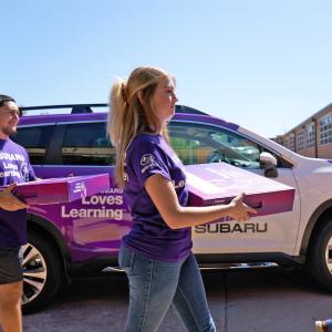 Three adults carrying boxes that say "Subaru Loves Learning"