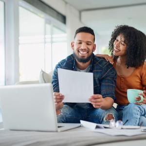 Smiling couple sitting on couch and looking at a piece of paper together