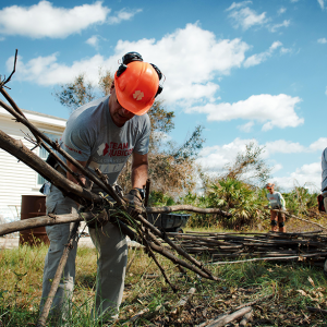 Three people in orange hardhats cleaning up debris