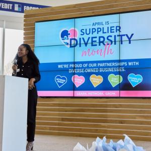 Woman speaking at a lectern in front of a sign reading, Supplier Diversity Month