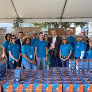 A group of people standing behind a table full of bobbleheads in boxes, pallets of boxes behind them.
