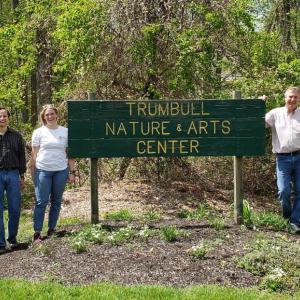 People stood either side of a sign that reads "Trumbull Nature and Arts Center"