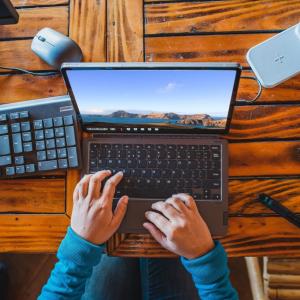 A pair of hands working on a laptop on a wooden table