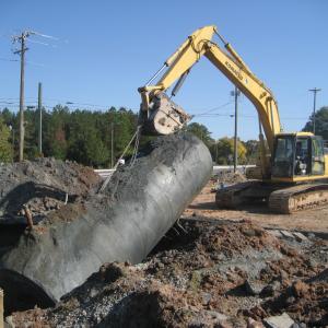 A yellow construction vehicle pulls a corroded UST out of the ground.