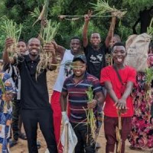A group of smiling people posed outside, holding plants.