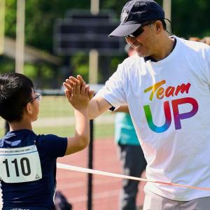 An adult wearing a Team UP shirt helping an athlete.