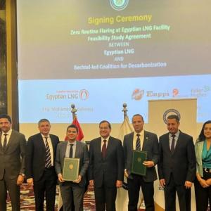 A line of people at a "signing ceremony" Some holding official documents. A large screen behind them.